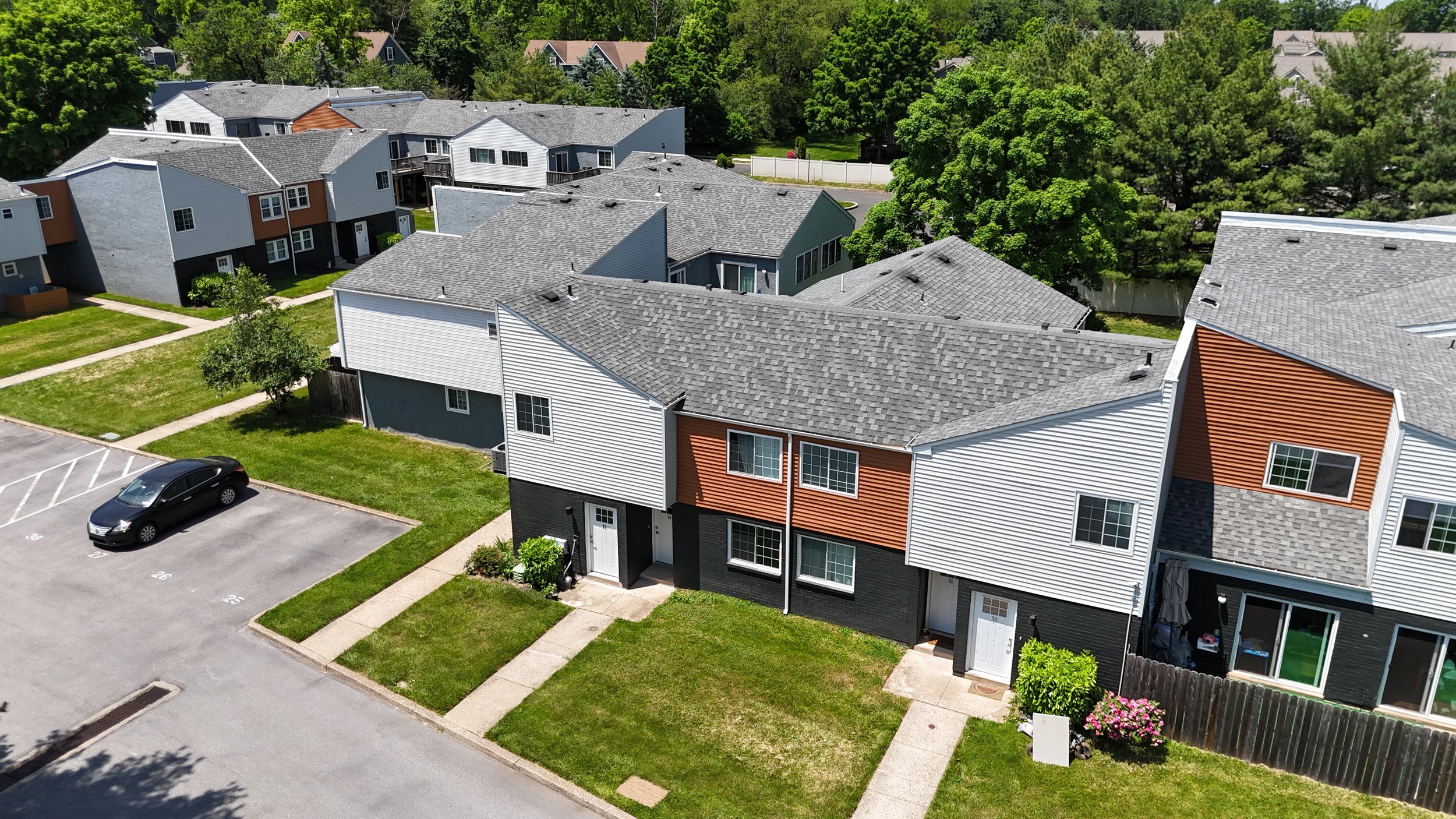 Aerial view of a residential area featuring multi-story townhouses with diverse color palettes and lush greenery. The scene highlights community living.