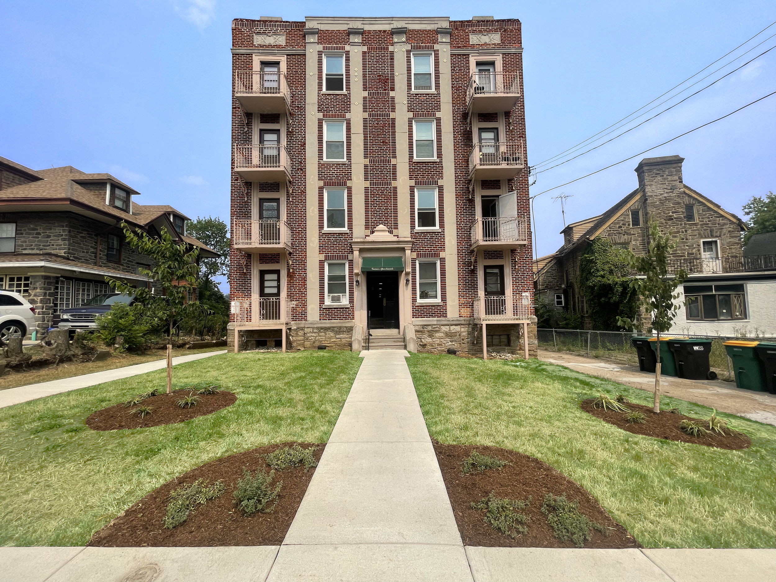 Newly renovated brick apartment building with balconies, surrounded by freshly landscaped grass and flower beds, creating an inviting community atmosphere.