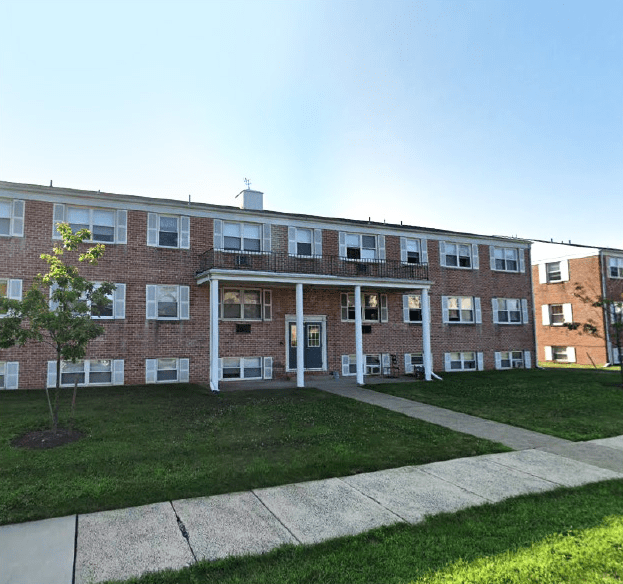 Brick apartment building with multiple windows, a central entrance, and a grassy area in front. Ideal for housing options in the area.