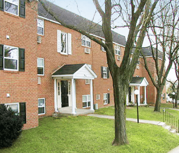 Brick apartment building featuring front porches and manicured lawns, set among trees. Ideal for showcasing residential properties or housing options.